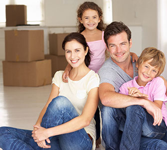 Smiling mother, father and two children sitting in new home with moving boxes behind them.